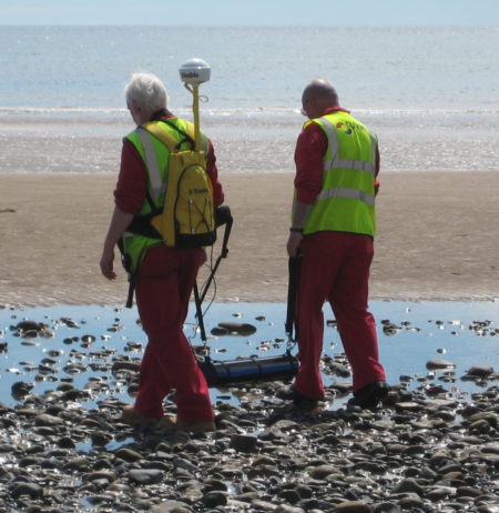 Two workers using a portable Gamma-Ray Spectrometer to monitor radiations on a beach