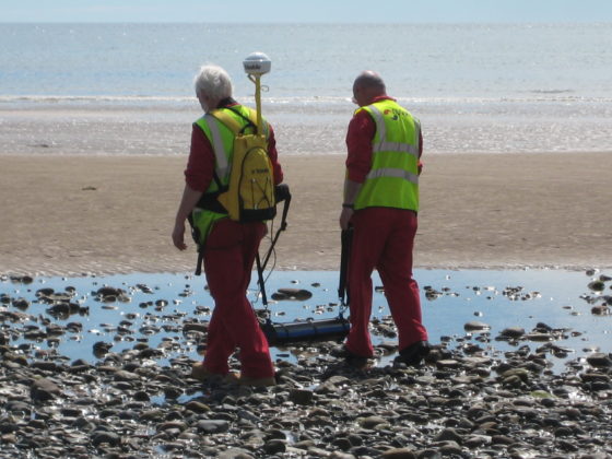 Two workers using a portable Gamma-Ray Spectrometer to monitor radiations on a beach