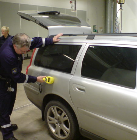 A ploiceman using a portable contraband detector on a car