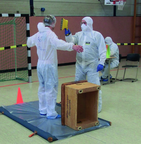 A person checking another's dose rate with a hand-held contamination monitor